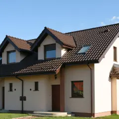 Nowy dom z beżową elewacją i brązowym dachem, otoczony zielonym trawnikiem.