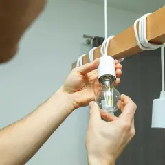 Ręce wkręcają żarówkę LED do drewnianego elementu lampy. Czy ledy się nagrzewają? Ta żarówka wygląda na chłodną.