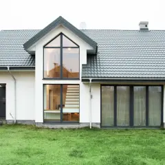 Nowoczesny dom wolnostojący z dużymi oknami i kamienną okładziną. W środku widać schody.