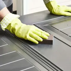 Manos enguantadas lijando una puerta para pintar aluminio.