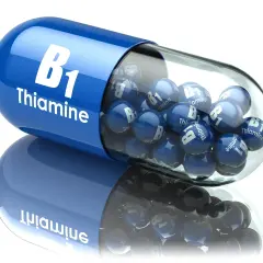 Niebieska kapsułka z napisem "B1 Thiamine" wypełniona małymi kulkami z tym samym oznaczeniem. Tiamina w pigułce.