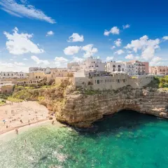 Vue panoramique de la plage de Polignano a Mare, avec ses falaises rocheuses, ses eaux turquoise et ses maisons blanches perchées.