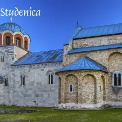 Kamienne mury i niebieskie dachy monastyru Studenica wznoszą się na tle zielonych wzgórz.