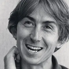 Black and white close-up portrait of Mark Hollis of Talk Talk smiling with his hand near his face.