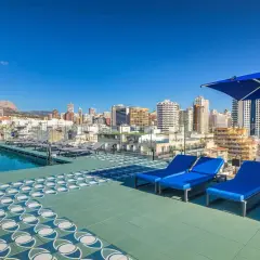 Terraza con piscina y tumbonas azules en Barceló Benidorm, con vistas a la ciudad y montañas.