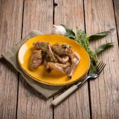 Sabroso conejo al ajillo servido en plato amarillo, acompañado de hierbas frescas y un tenedor, sobre una mesa de madera rústica.