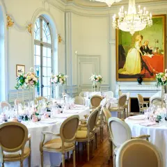 Salle de réception élégante avec tables rondes dressées pour un mariage. Un tableau ancien domine la pièce, offrant une idée de plan de table mariage.