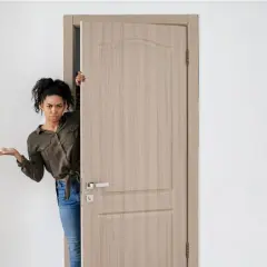 Mujer asomándose por una puerta de madera clara, con expresión de duda. Los colores de puertas son neutros y elegantes.