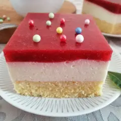 Pyszna żelka truskawkowa z mrożonych truskawek, z kremową warstwą i biszkoptem, ozdobiona kolorowymi kuleczkami.