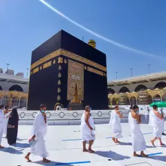 Pielgrzymi w białych strojach okrążają Kaabę, święte miasto islamu, w słoneczny dzień.