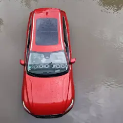 Czerwony samochód stoi w wodzie. Po powodzi czeka go osuszanie auta.
