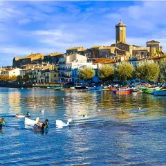 Anatre nuotano in un lago sereno, con un borgo pittoresco e barche colorate che si specchiano sull'acqua. Un'immagine da cartolina dei laghi italiani.