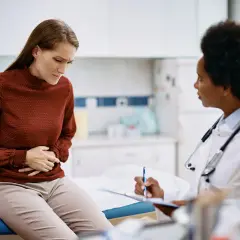 Frau mit Bauchschmerzen spricht mit Ärztin über mögliche Porphyrie Symptome.