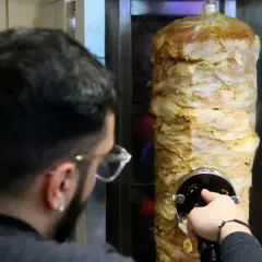 Mężczyzna kroi mięso z pionowego rożna na kebab.