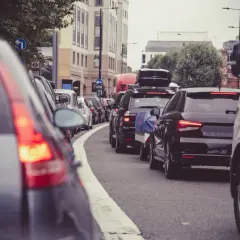 Korek w mieście, gdzie jest ruch lewostronny. Samochody stoją w rzędzie, widać znaki drogowe i budynki.