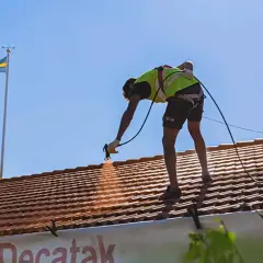 Arbetare sprutmålar tak med svensk flagga i bakgrunden.