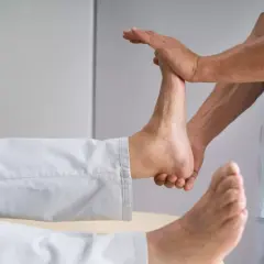 Fizjoterapeuta wykonuje ćwiczenia na opadającą stopę, delikatnie unosząc ją.