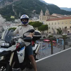 Motociclista in sella alla sua BMW, ammira il panorama della meta costiera amalfitana con le case aggrappate alla montagna.