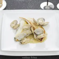 Coruxo pescado con almejas en salsa cremosa, servido en plato blanco.
