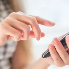 Dłonie obsługują smartfon, palce przesuwają się po ekranie, jakby wybierały opcję z menu +20 kierunkowego.