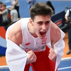Młody lekkoatleta w biało-czerwonej koszulce okryty białą flagą, krzyczy z radości po zwycięstwie na halowych mistrzostwach europy lekkoatletyka.