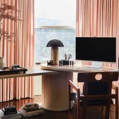 Stylish personal office decor ideas: a modern desk with a computer, lamp, and plant, framed by soft pink curtains.