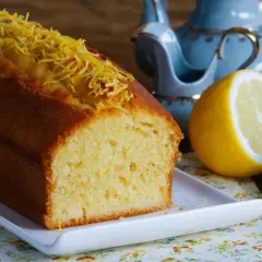 Puszysta babka cytrynowa, ozdobiona skórką cytrynową, czeka na herbatę z błękitnego serwisu.