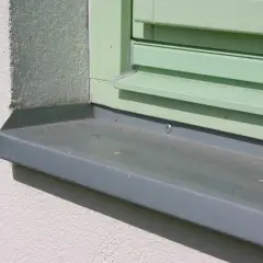 Szary, metalowy parapet zewnętrzny pod zielonym oknem, idealnie chroniący elewację.