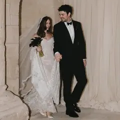Novia con velo y ramo de **stella banderas** negras, y novio de traje, saliendo de una iglesia.