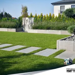 Nowoczesny ogród z prostymi, betonowymi płytami chodnikowymi w trawie, otoczony geometrycznymi donicami i bujną zielenią.