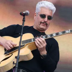 Un cantautore napoletano famoso con capelli bianchi e occhiali da sole suona una chitarra jazz.