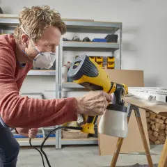 Uomo con maschera usa una vernice per pistola a spruzzo per dipingere un telaio bianco su un tavolo da lavoro.
