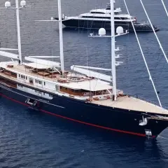 Il maestoso yacht Koru, con i suoi lussuosi interni, naviga in acque blu. Un altro yacht più piccolo è visibile sullo sfondo.