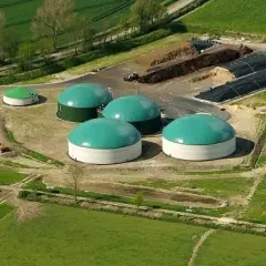 Impianto di biogas con grandi serbatoi verdi e bianchi, cumuli di materiale organico e serre. Un esempio di incentivi biogas per l'energia rinnovabile.