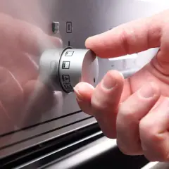 Hand dreht am Drehregler des Ofens, um die Grillfunktion auszuwählen.