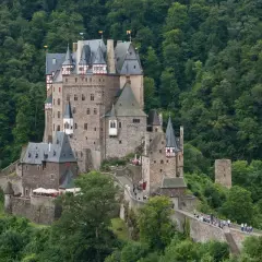 Burg Eltz, ett sagoslott omgivet av grönskande skog, reser sig stolt på en klippa. Många besökare vandrar längs murarna.