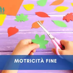 Mani di bambino che ritagliano forme di foglie colorate con forbici rosa, un'attività per sviluppare la motricità fine.