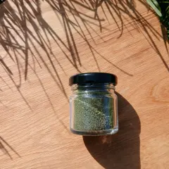 Un piccolo barattolo di vetro contiene polvere di ortica verde brillante, posato su un tagliere di legno con ombre di foglie.
