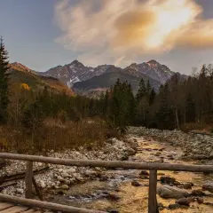 Jesienne Tatry w październiku. Drewniany mostek nad kamienistym potokiem, w tle góry i lasy.