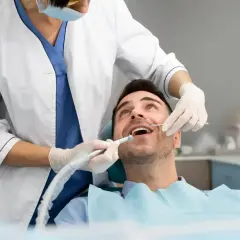 Pacjent uśmiecha się, gdy dentysta wykonuje zabieg. **Sedacja u dentysty** sprawia, że wizyta jest komfortowa i bezstresowa.