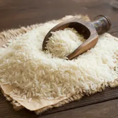 Ein Holzlöffel schöpft weißen Langkornreis aus einem Haufen auf Jute. Der Unterschied zwischen Basmati-Reis und Langkornreis ist hier visuell dargestellt.