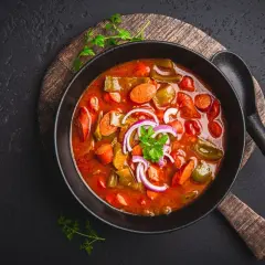 Gęsta, aromatyczna solanka z kiełbasą, papryką i cebulą, podana w czarnej misce na drewnianej desce.