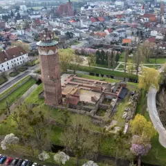 Ruiny zamku krzyżackiego w Brodnicy z charakterystyczną wieżą, otoczone zielenią i wodą, w tle rozciąga się miasto.