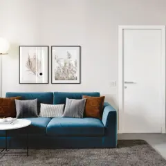 Divano blu intenso con cuscini tortora e grigi. Un tavolino bianco e un tappeto scuro completano l'ambiente.
