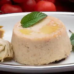 Delizioso flan di carciofi, guarnito con menta e accompagnato da carciofi sott'olio, pomodori secchi e capperi.