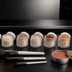 Barattoli di polveri per makeup: amido, caolino, argilla rosa, mica, ossidi colorati. Pennelli e blush in polvere.