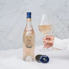 Une main tient un verre de vin rosé, à côté d'une bouteille et de caviar. Le danger du vin rosé est qu'il est si délicieux qu'on en redemande.
