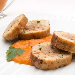 Rollo de bonito cortado en rodajas, servido sobre puré de pimientos y decorado con perejil.