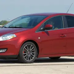 Czerwony Fiat Bravo z kierowcą za kierownicą, zaparkowany na zewnątrz.