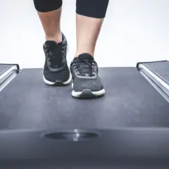 Nogi w sportowych butach stawiają pierwsze kroki na bieżni w bloku.